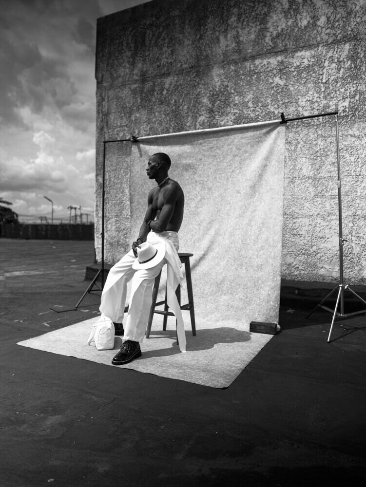 Black-and-white portrait of a man seated on a stool against a backdrop on a rooftop
