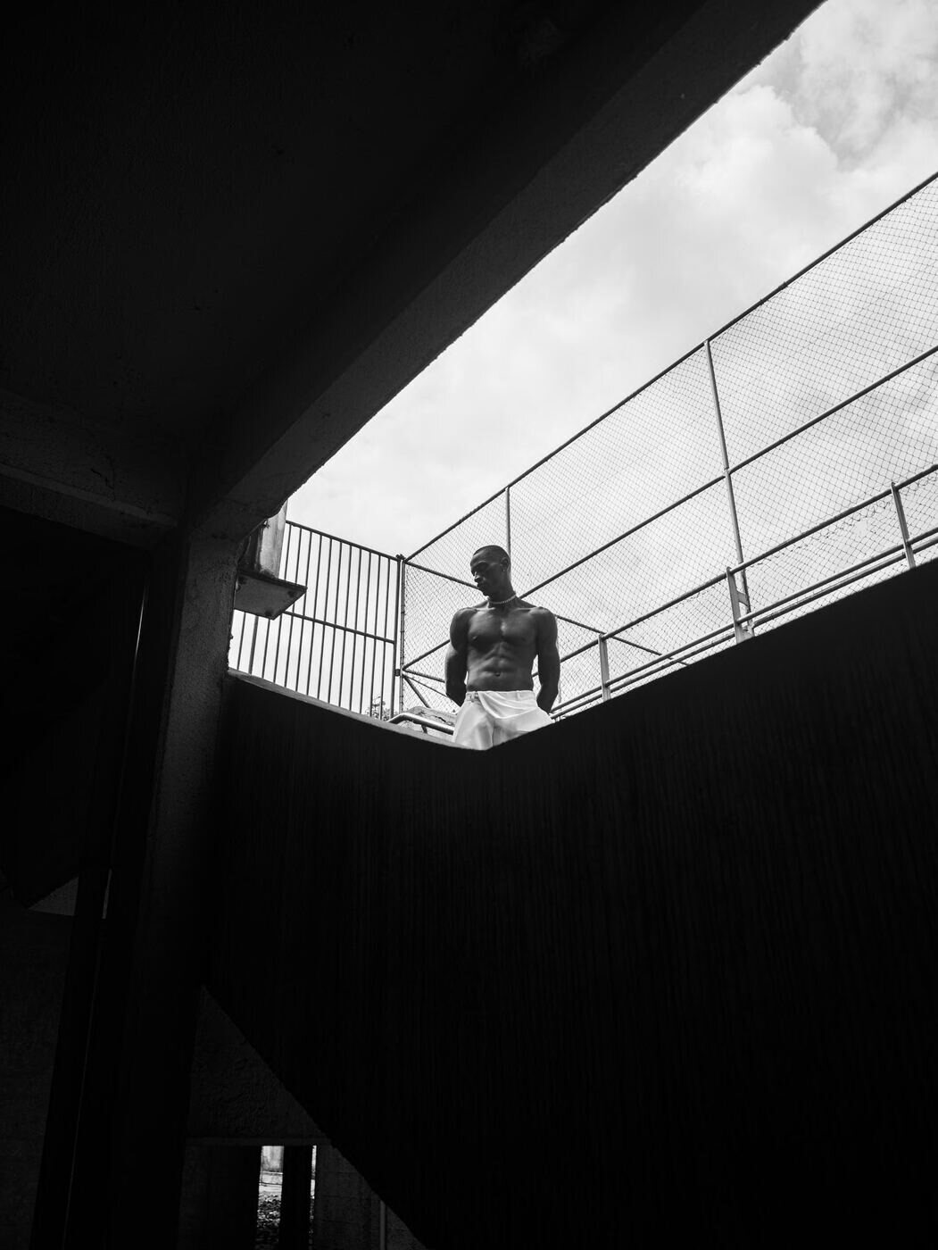 Black-and-white figure framed by a hard diagonal of shadow and railings